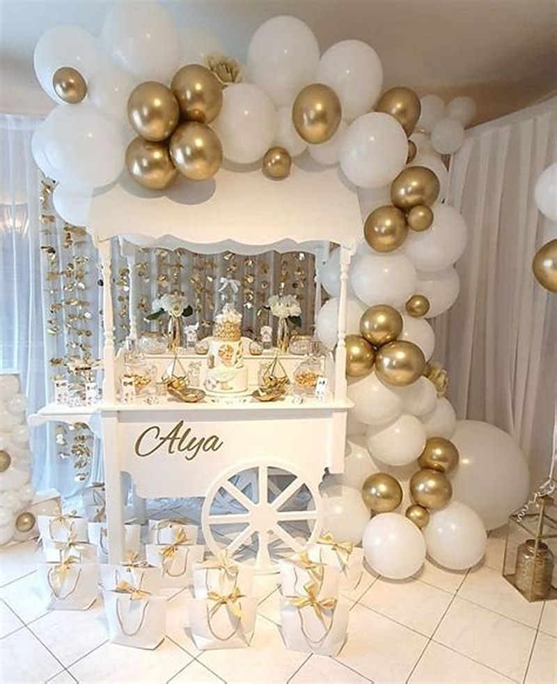 Chariot de douceurs blanc au prénom de l'enfant, entouré d'une arche de ballons blancs et or.