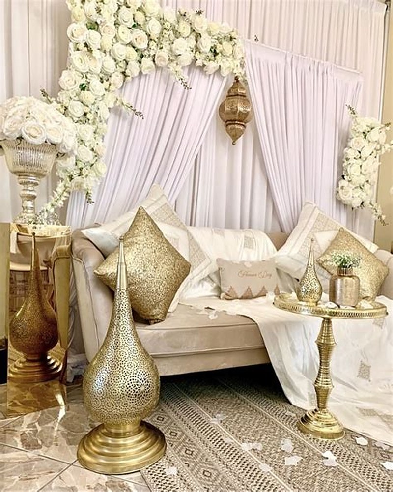 Salon oriental blanc et or : banquette, coussins brodés, lanternes dorées et arche florale blanche.